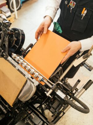 A person binding an orange book with craft equipment in a studio.