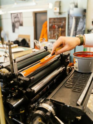 Close-up of a vintage printing press with a hand applying ink, showcasing traditional printing techniques.